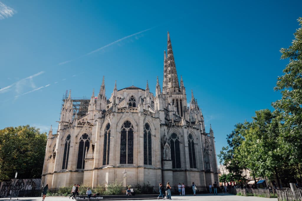 Cathédrale Saint-André de Bordeaux : architecture gothique Cathédrale gothique Saint-André de Bordeaux, majestueuse sous un ciel bleu clair avec des traînées de condensation et des échafaudages sur une flèche.