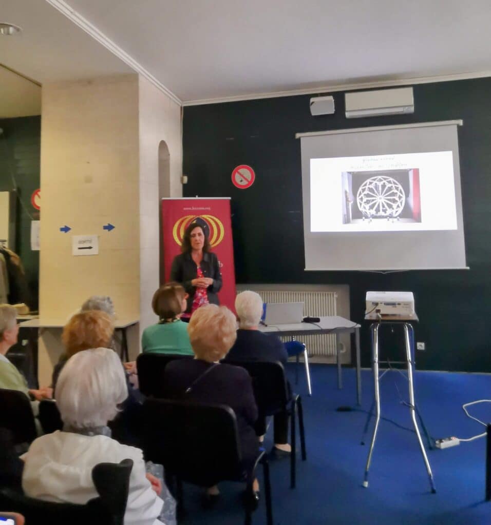 Conférence rosace gothique : présentation d'art Conférence sur l'art ou l'architecture avec une femme parlant devant un écran projetant une rosace gothique. Public assis. Panneau "SORTIE" visible.
