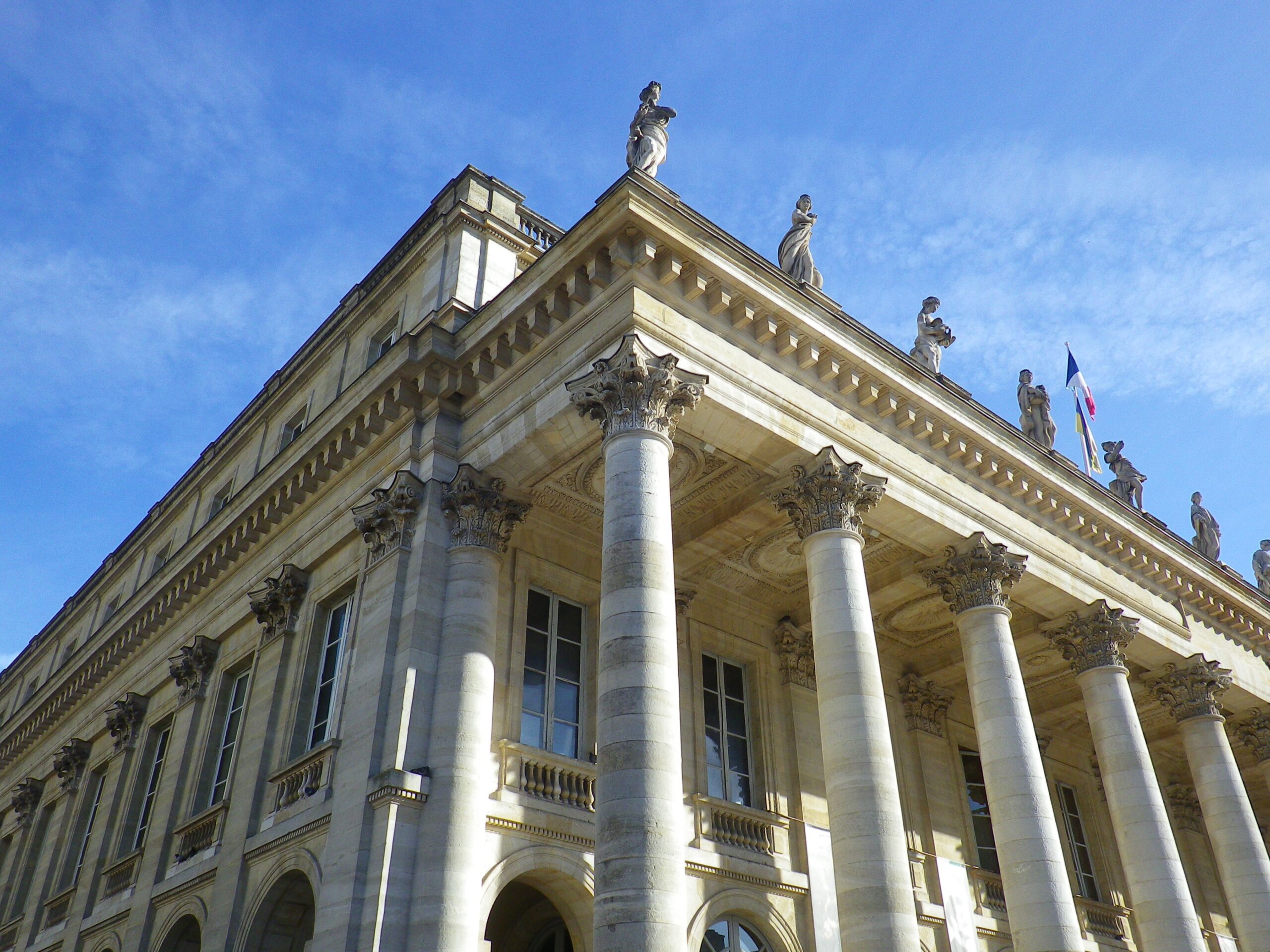 Femme souriante vêtue de noir devant un bâtiment parisien Portrait souriant d'une femme aux cheveux bruns, vêtue d'une veste noire sur une robe violette, devant un bâtiment de style haussmannien.